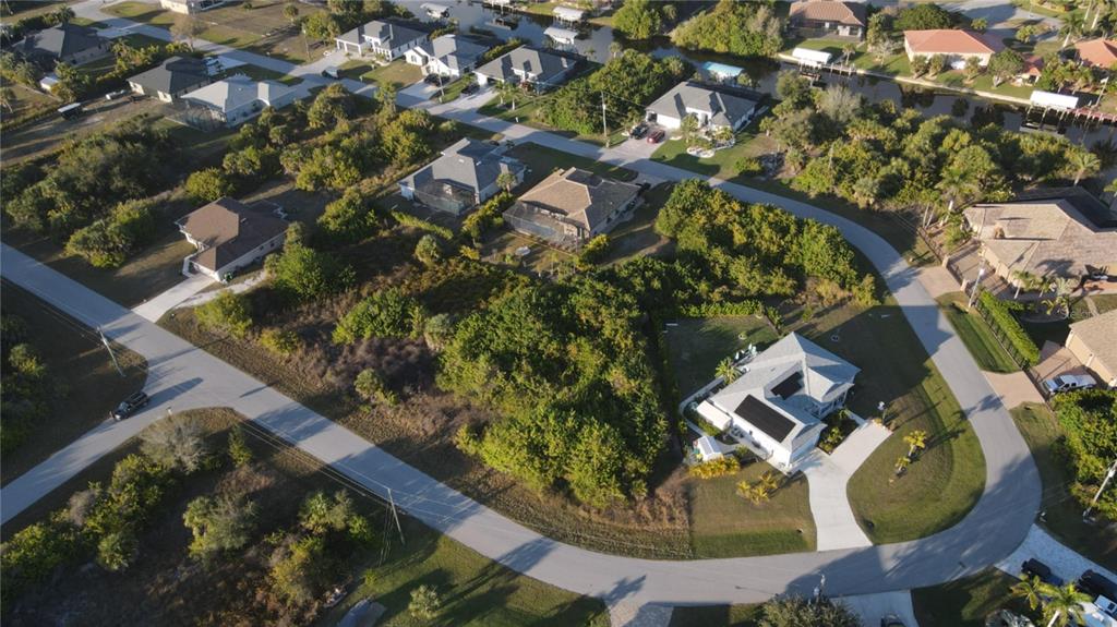 An aerial view shows a suburban neighborhood with several houses and wooded lots — 9399 PANAMA CIRCLE, PORT CHARLOTTE, FL