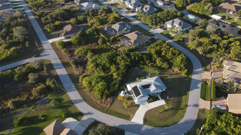 An aerial view shows a suburban neighborhood with houses, paved roads, and dense vegetation — 9399 PANAMA CIRCLE, PORT CHARLOTTE, FL