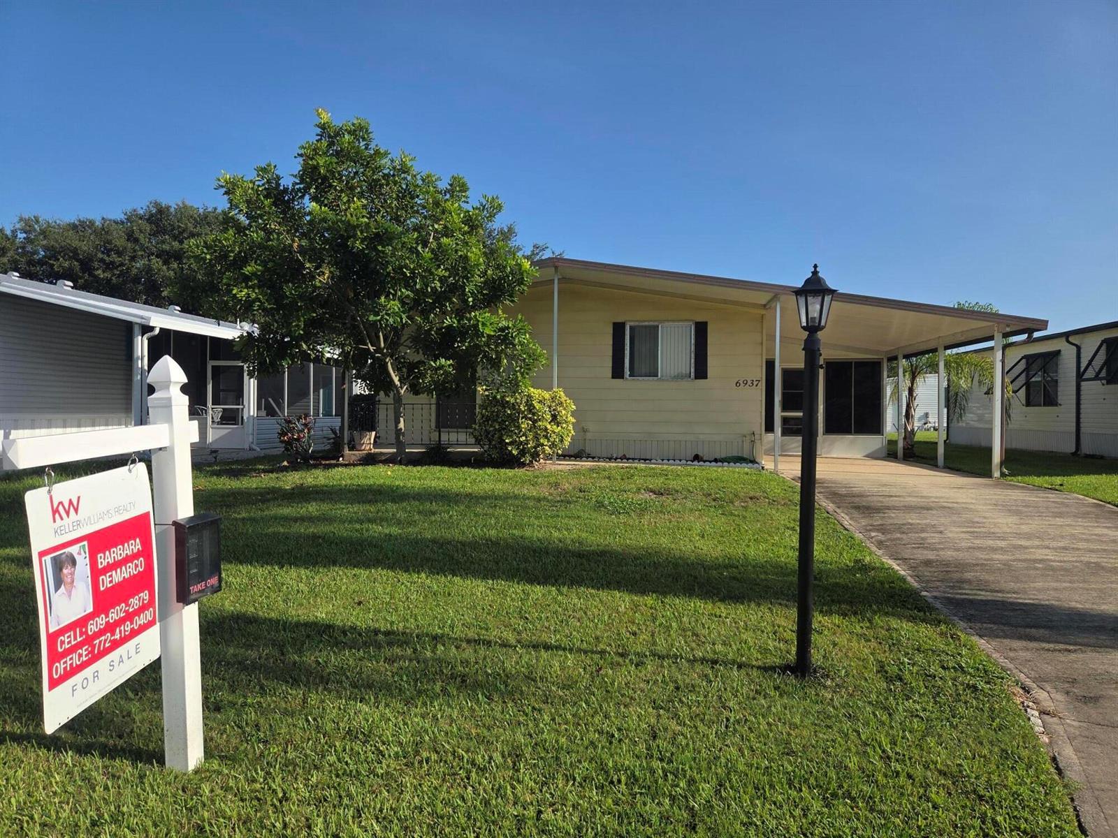 A single-story mobile home with a carport and a real estate sign in the yard — 6937 SE Delegate Street, Hobe Sound FL 33455, HOBE SOUND, FL