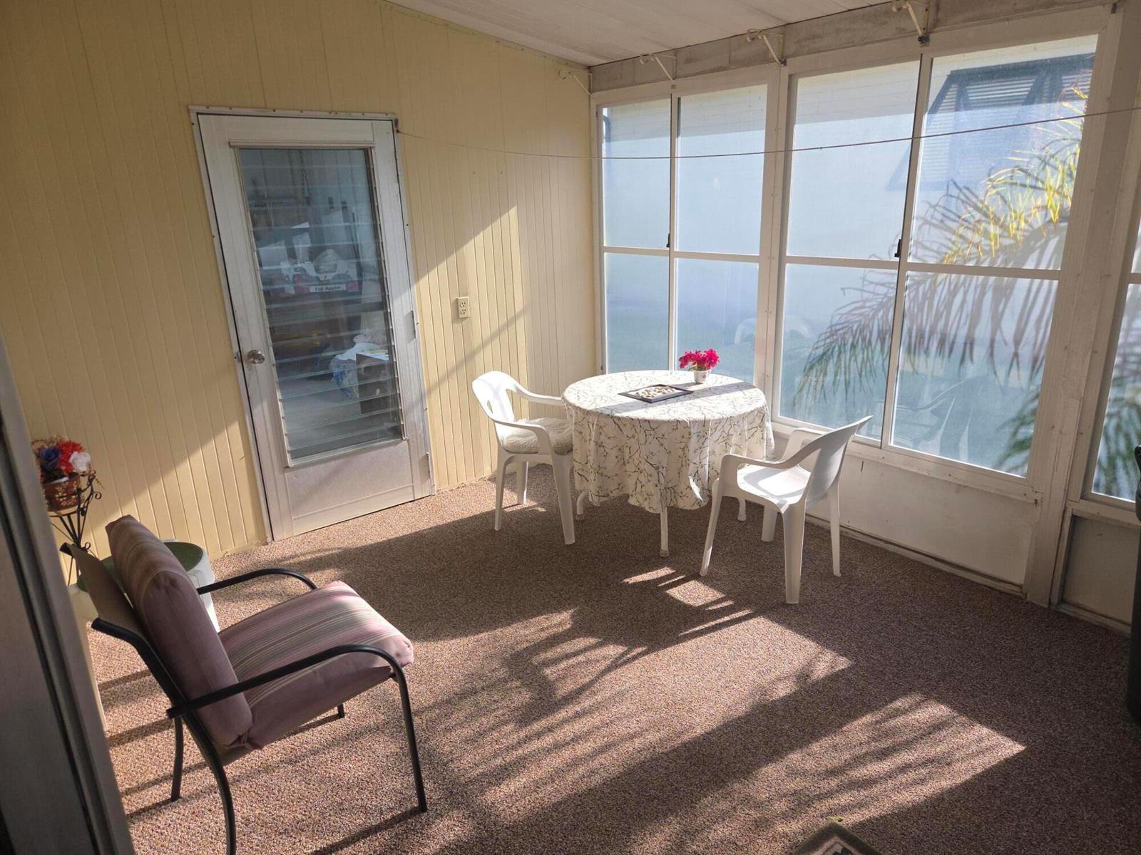 A sunroom features yellow paneled walls, carpeted flooring, a small dining set, and large windows — 6937 SE Delegate Street, Hobe Sound FL 33455, HOBE SOUND, FL