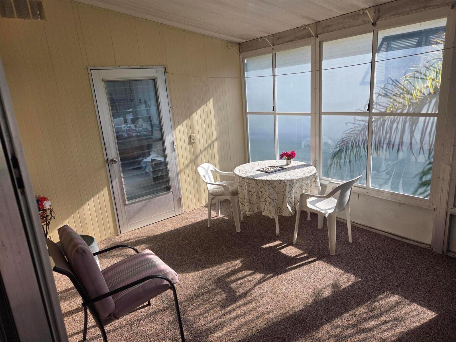 A sunroom features a round table with two chairs, carpeted flooring, and large window panels — 6937 SE Delegate Street, Hobe Sound FL 33455, HOBE SOUND, FL