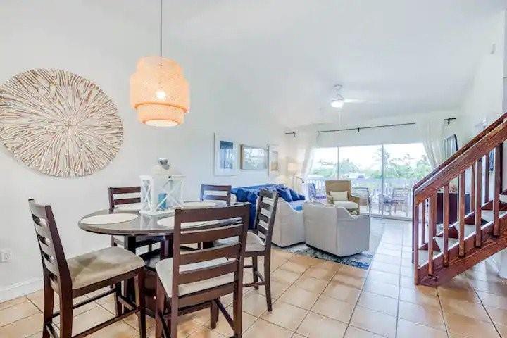 A dining area with a round table and chairs sits beside a living room with stairs — 164 Ocean Bay Drive # c, Key Largo FL 33037, KEY LARGO, FL