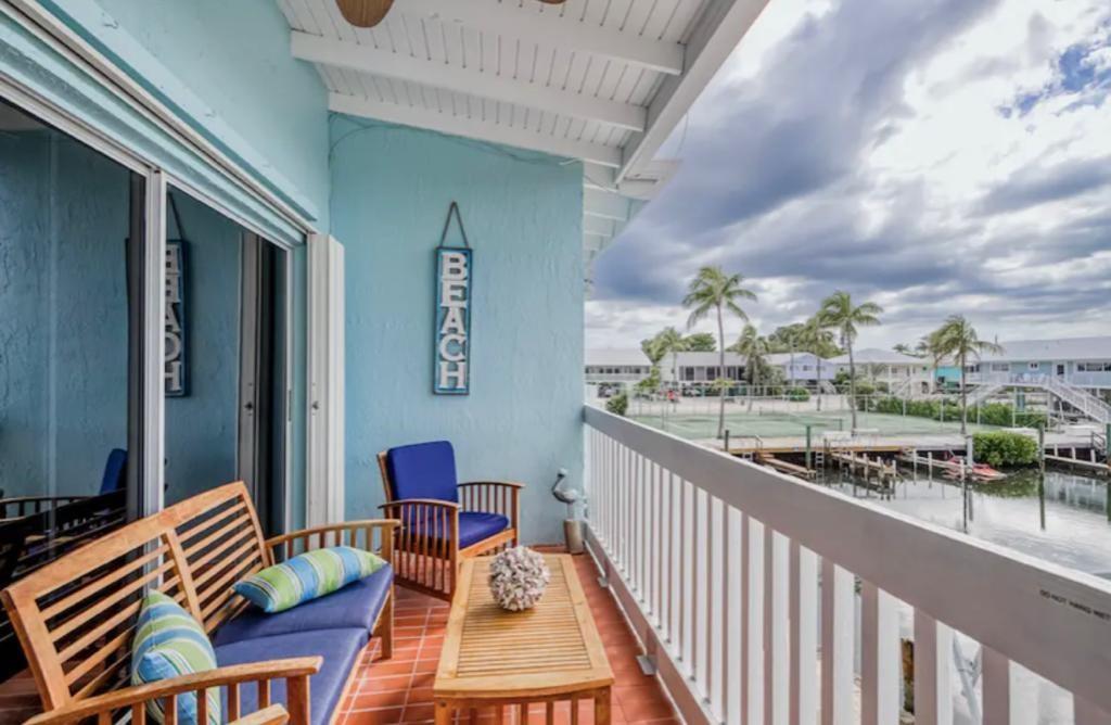 A balcony with wooden furniture overlooks a tennis court and a canal with boat docks — 164 Ocean Bay Drive # c, Key Largo FL 33037, KEY LARGO, FL