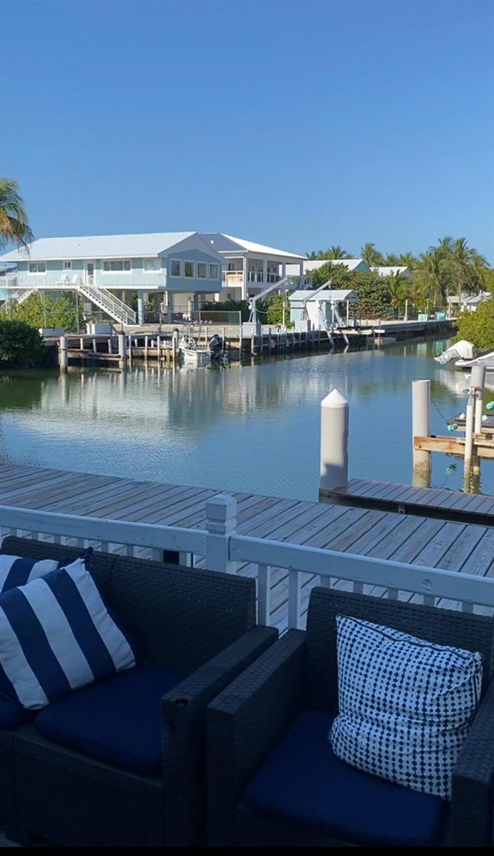 A view from a deck with outdoor seating overlooking a canal and waterfront houses — 164 Ocean Bay Drive # c, Key Largo FL 33037, KEY LARGO, FL
