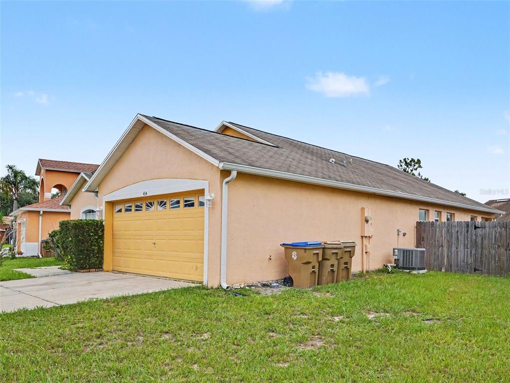 A peach-colored house exterior features a yellow garage door and three trash bins outside — 414 SPICE COURT, KISSIMMEE, FL