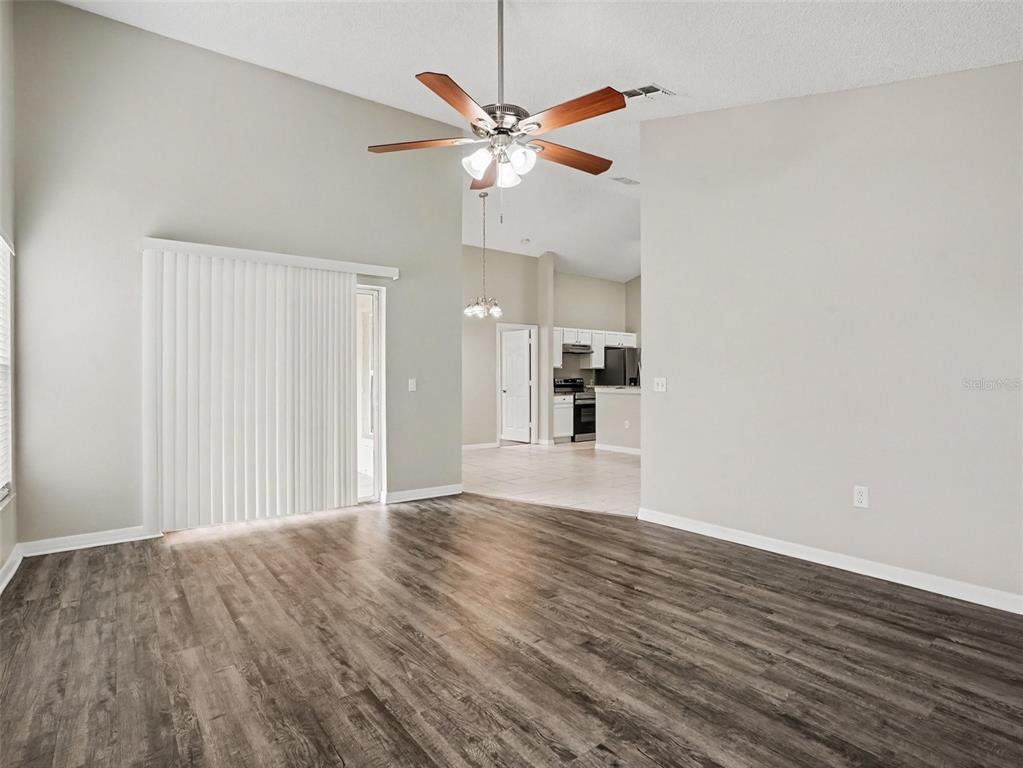 A living room with wood-look flooring, vaulted ceilings, a ceiling fan, and a sliding glass door — 414 SPICE COURT, KISSIMMEE, FL