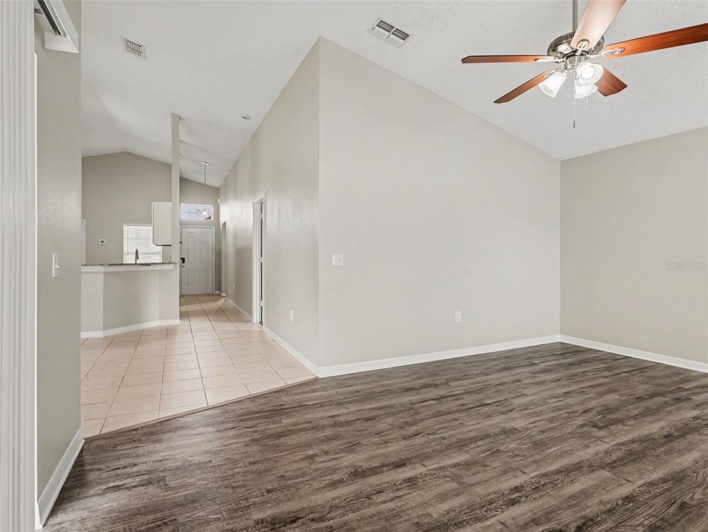 A living room with wood-look flooring transitions to a tiled kitchen area with vaulted ceilings — 414 SPICE COURT, KISSIMMEE, FL