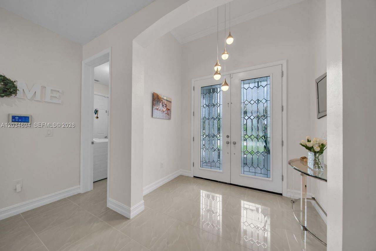 A bright entryway features white walls, tile flooring, double glass-paneled doors, and a pendant light — 60 Floyd Ave S, Lehigh Acres FL 33976, LEHIGH ACRES, FL