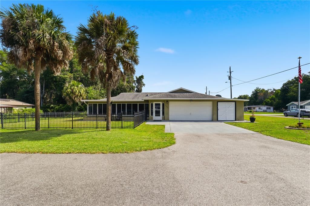 A single-story house with a screened porch, two-car garage, and palm trees in the yard — 1381 CR 446A, LAKE PANASOFFKEE, FL