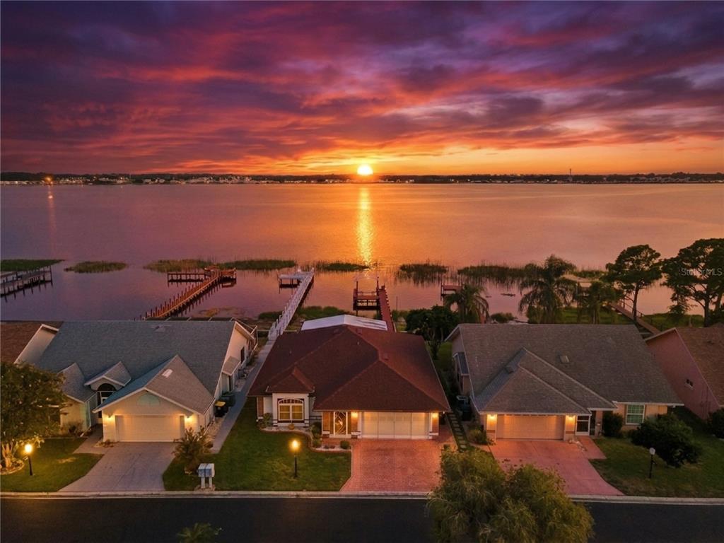 An aerial view of three waterfront houses at sunset with private docks extending into the lake — 452 SWEETWATER WAY, HAINES CITY, FL