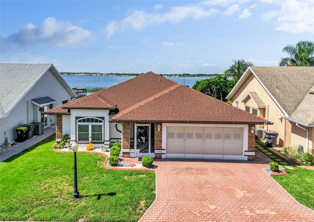 An exterior view of a single-story house with a brick driveway and a lake view — 452 SWEETWATER WAY, HAINES CITY, FL