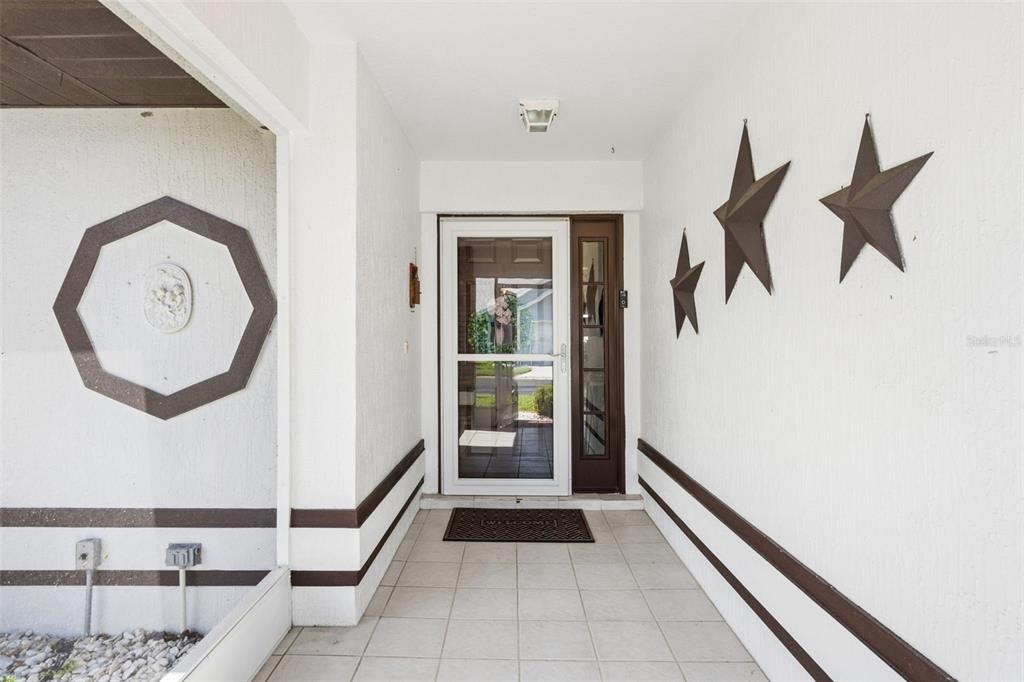 A covered entryway features a tiled floor, white walls with brown trim, and metal star decorations — 452 SWEETWATER WAY, HAINES CITY, FL