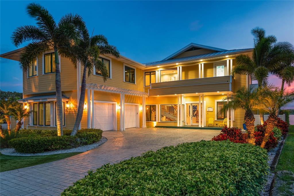 A two-story yellow house with a paved driveway, palm trees, and exterior lighting at dusk — 2012 SPYGLASS LANE, NEW SMYRNA BEACH, FL