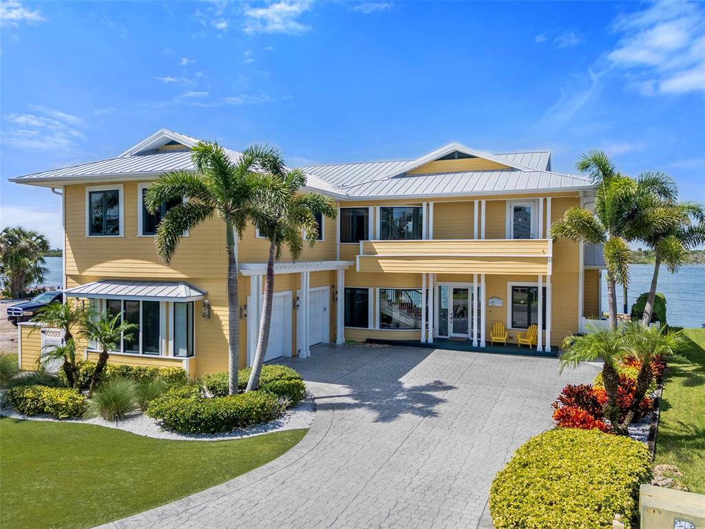 A yellow two-story waterfront house features a stone patio, a wooden dock, and large windows — 2012 SPYGLASS LANE, NEW SMYRNA BEACH, FL