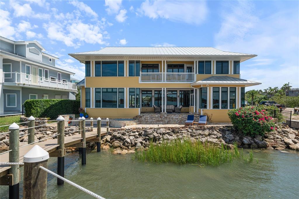 A two-story yellow house with a metal roof, stone patio, and a wooden boat dock — 2012 SPYGLASS LANE, NEW SMYRNA BEACH, FL