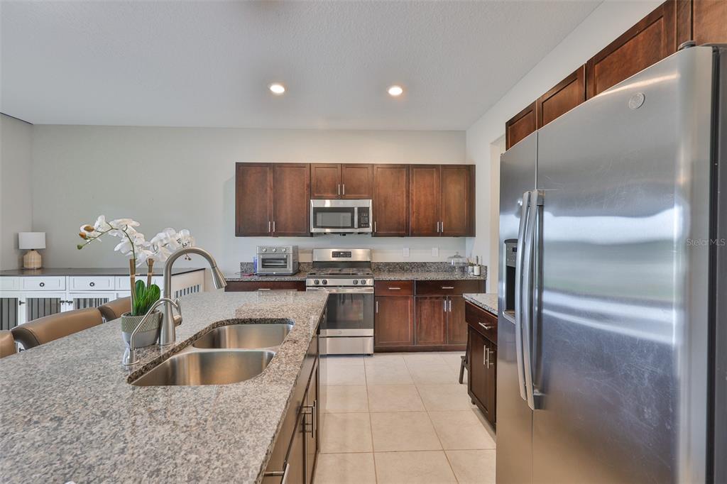 A kitchen features dark wood cabinets, granite countertops, stainless steel appliances, and a large island — 9454 CHANNING HILL DRIVE, SUN CITY CENTER, FL