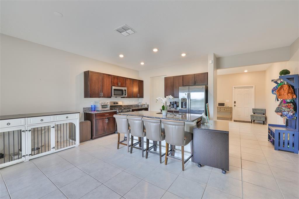 A kitchen features dark wood cabinetry, a granite-topped island with bar stools, and tile flooring — 9454 CHANNING HILL DRIVE, SUN CITY CENTER, FL