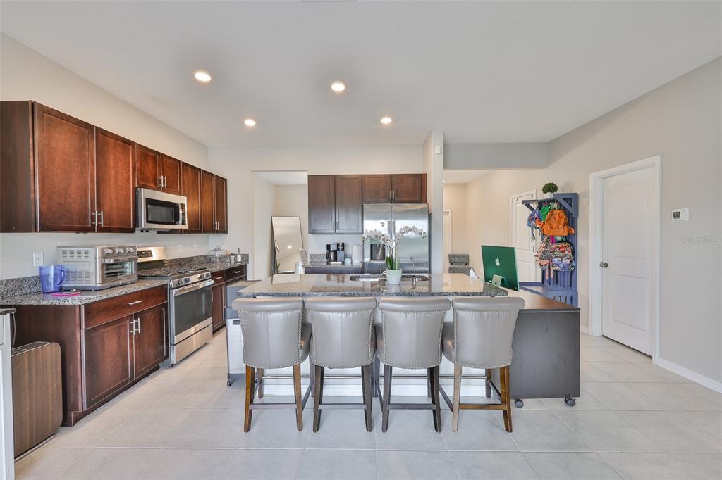 A kitchen features dark wood cabinets, granite countertops, stainless steel appliances, and a central island — 9454 CHANNING HILL DRIVE, SUN CITY CENTER, FL