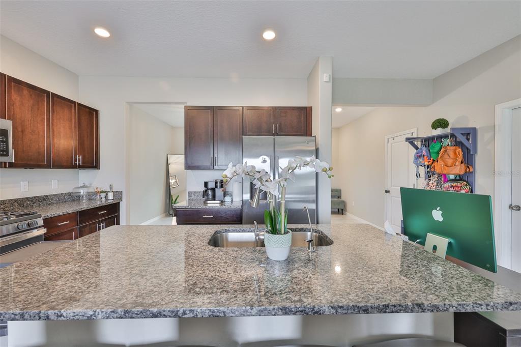 A kitchen features dark wood cabinets, granite countertops, a central island, and stainless steel appliances — 9454 CHANNING HILL DRIVE, SUN CITY CENTER, FL
