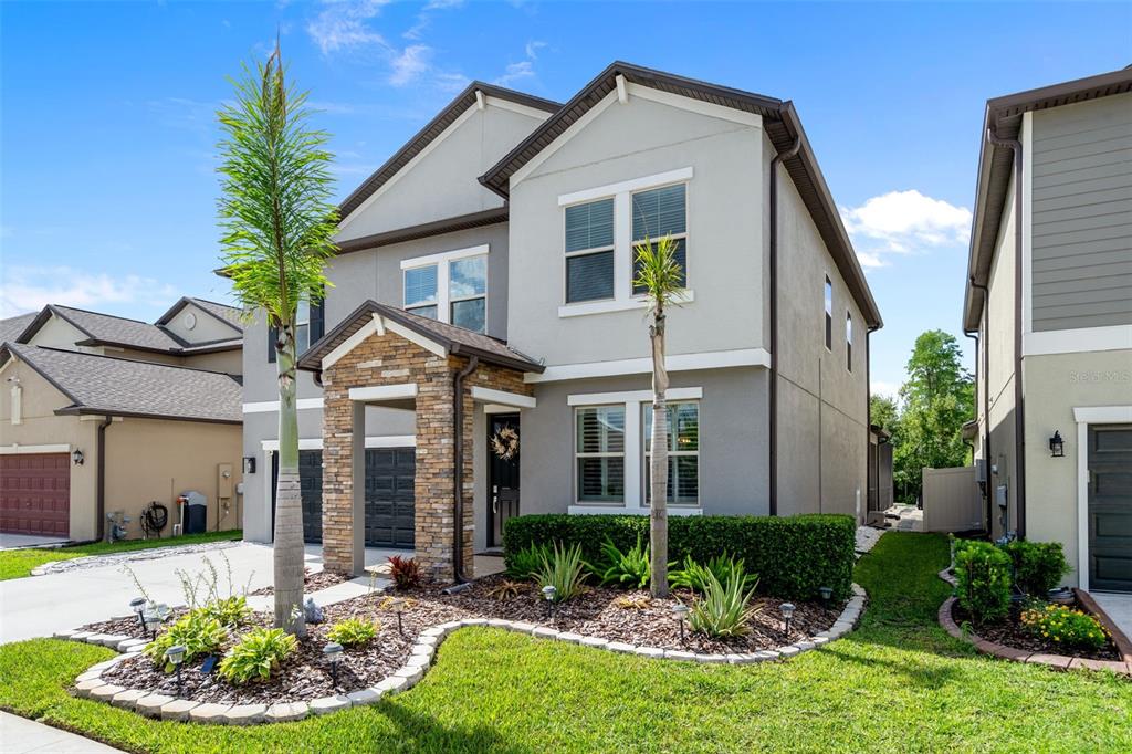 A two-story suburban house with a stone-accented entryway, gray stucco siding, and landscaped front yard — 8755 FLOURISH DRIVE, LAND O LAKES, FL