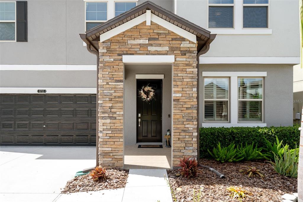 A stone-accented entryway leads to a black front door next to a dark garage — 8755 FLOURISH DRIVE, LAND O LAKES, FL