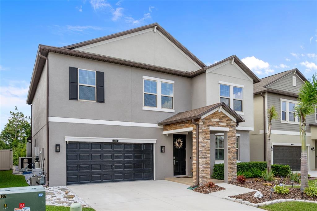 A two-story house with a gray stucco exterior, stone-accented entryway, and a two-car garage — 8755 FLOURISH DRIVE, LAND O LAKES, FL