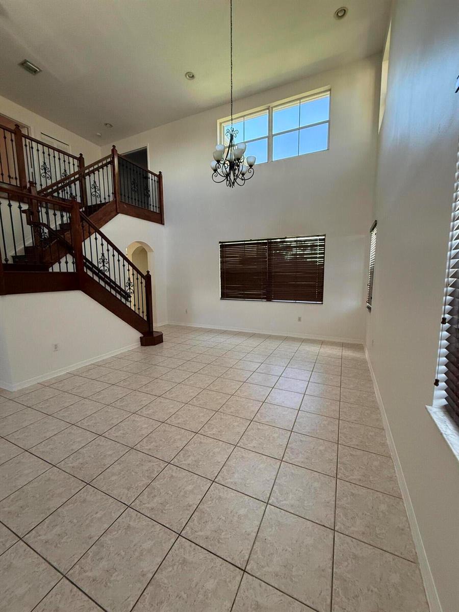 A two-story foyer features tile flooring, a wooden staircase, and a large chandelier — 12631 SW 28th Street, Miramar FL 33027, MIRAMAR, FL