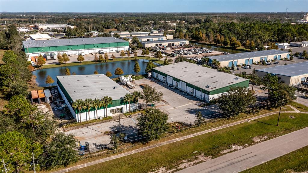 An aerial view shows several industrial warehouse buildings with metal roofs near a retention pond — 1770 BUSINESS CENTER LANE, KISSIMMEE, FL