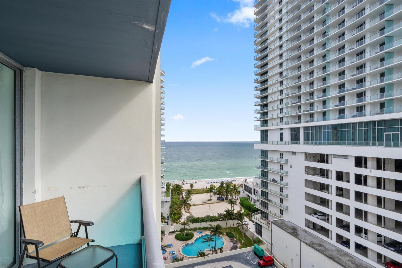 A balcony with a chair overlooks a swimming pool, beach, and a large high-rise building — 4001 S Ocean Drive # 14D, Hollywood FL 33019, HOLLYWOOD, FL