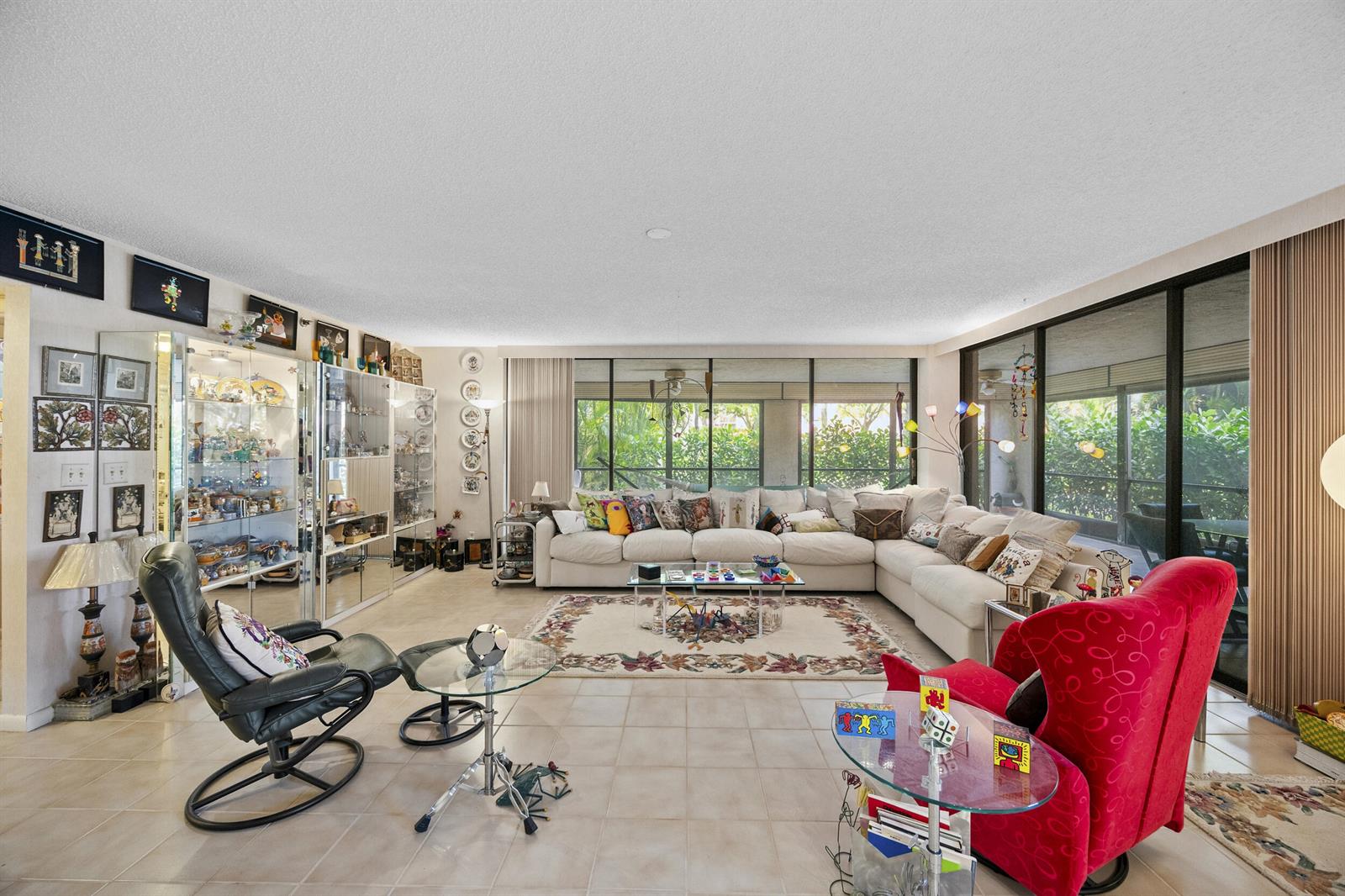 A spacious living room features a large sectional sofa, a red armchair, and glass display cabinets — 7209 Promenade Drive # 101, Boca Raton FL 33433, BOCA RATON, FL
