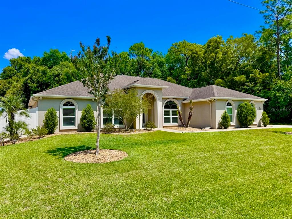 A single-story beige house with a hip roof and arched windows sits on a grassy lawn — 8353 SE 162ND STREET, SUMMERFIELD, FL
