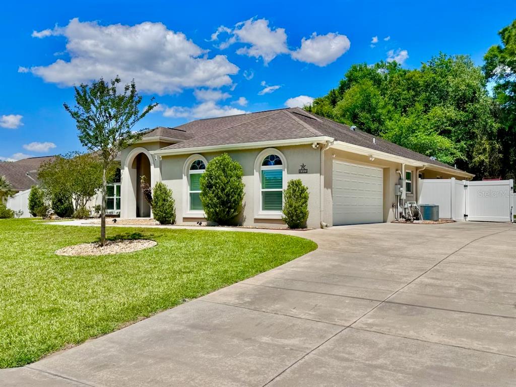 A single-story house with a beige stucco exterior, a concrete driveway, and a two-car garage — 8353 SE 162ND STREET, SUMMERFIELD, FL