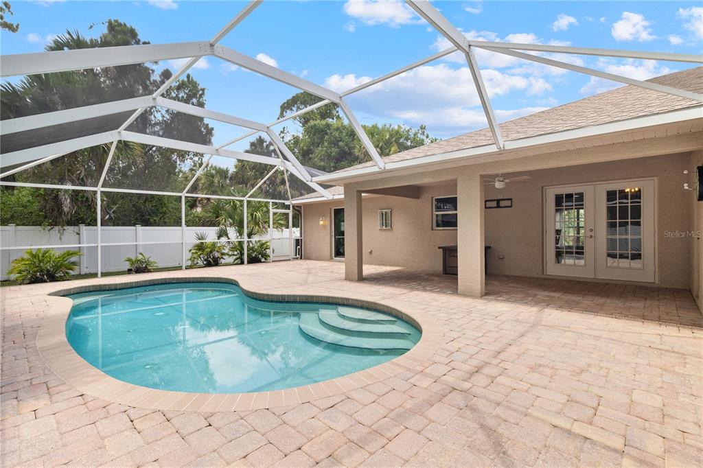 A screened-in patio features a kidney-shaped swimming pool and paver decking next to a house — 3941 SANTA ANA ROAD, NORTH PORT, FL
