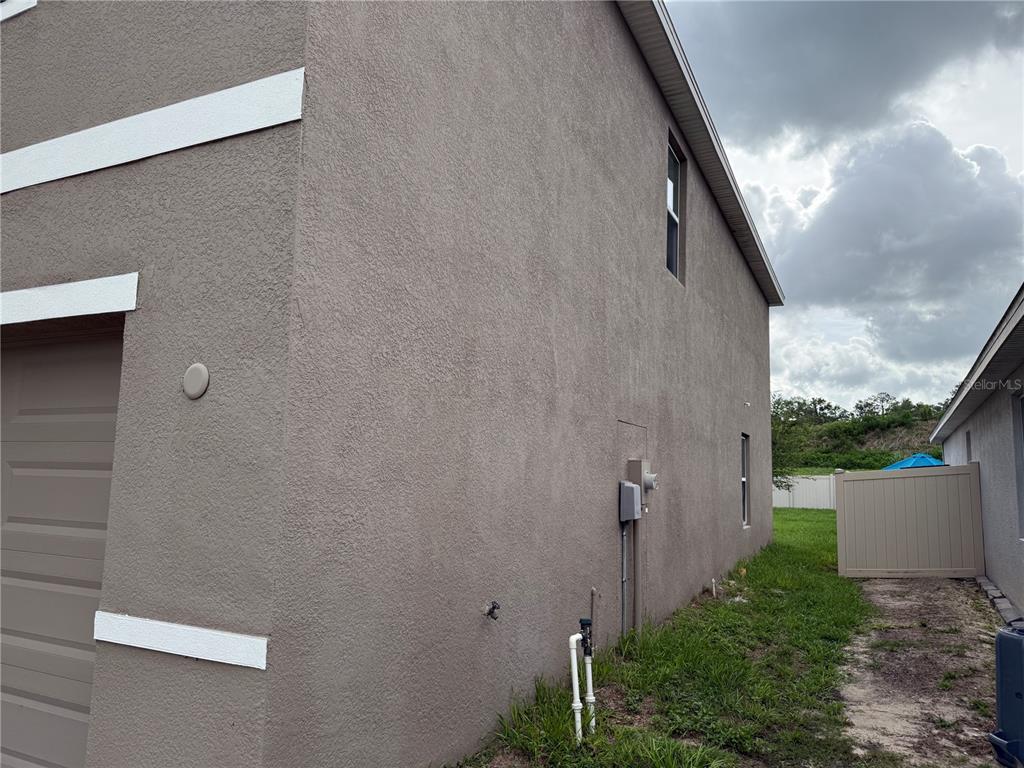 The exterior side view of a house shows a stucco wall, garage door, and utilities — 6616 SEAWAY DRIVE, BROOKSVILLE, FL