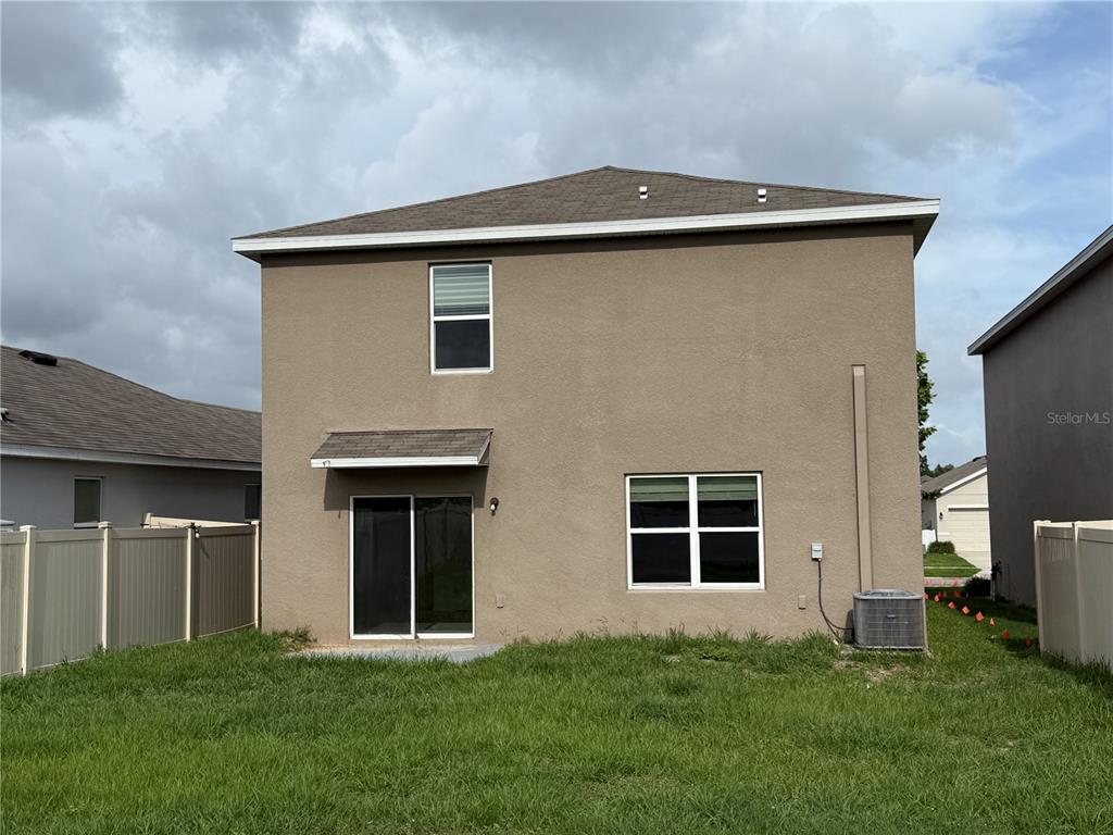 The back exterior of a two-story house features a sliding glass door and windows — 6616 SEAWAY DRIVE, BROOKSVILLE, FL