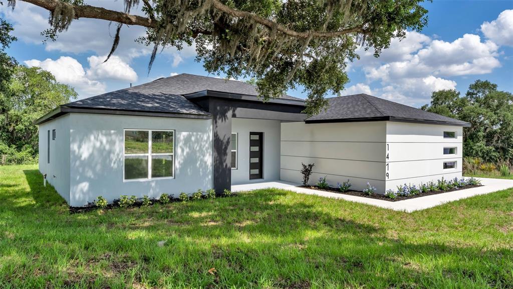 A modern, single-story house with a light-colored stucco exterior and dark trim sits on grass — 1479 HOLLY HILL ROAD, DAVENPORT, FL