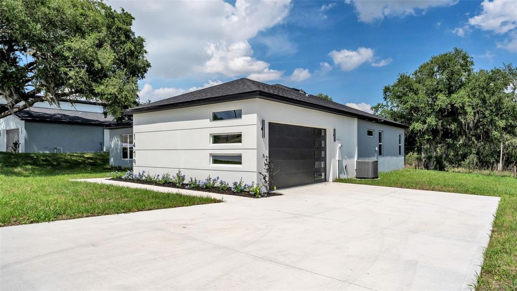 A modern white house with a dark garage door and horizontal windows sits on a lot — 1479 HOLLY HILL ROAD, DAVENPORT, FL