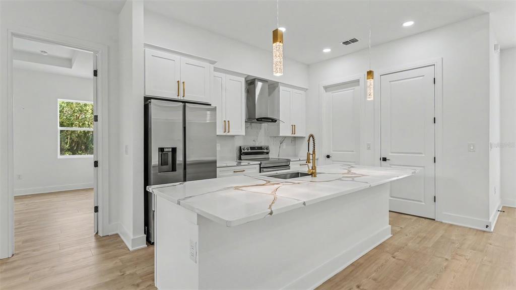 A modern white kitchen features a marble-topped island, stainless steel appliances, and gold hardware — 1479 HOLLY HILL ROAD, DAVENPORT, FL