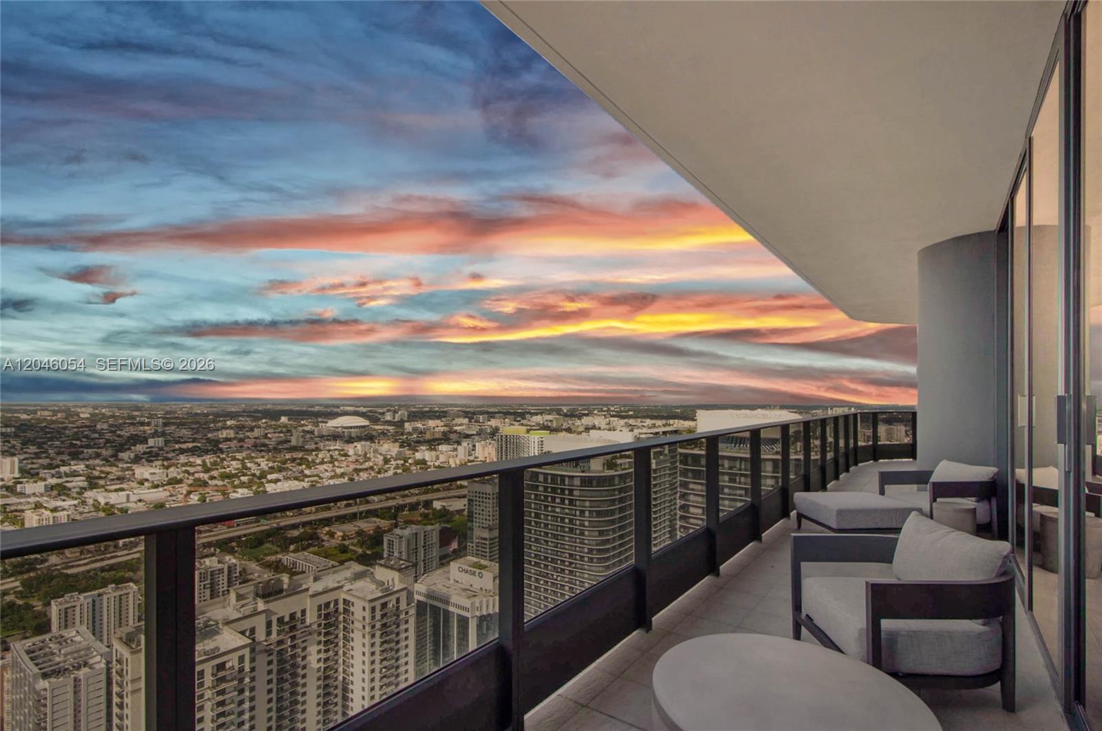 A high-rise balcony with outdoor seating overlooks a city skyline under a sunset sky — 1000 Brickell Plz, Miami FL 33131, MIAMI, FL