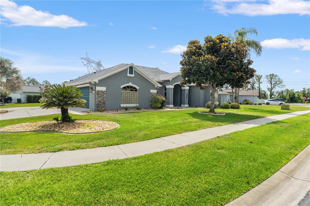 A gray single-story house with a stone-accented facade, a front lawn, and a large tree — 450 CASTILLE DRIVE, SPRING HILL, FL