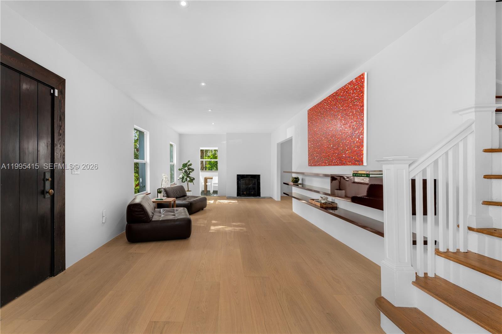 A living room features light wood flooring, a fireplace, a staircase, and a large painting — 5812 Alton Rd, Miami Beach FL 33140, MIAMI BEACH, FL