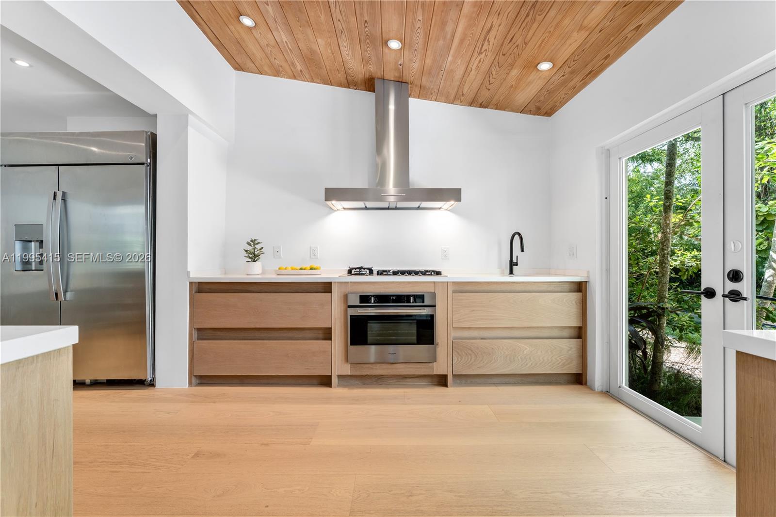 A modern kitchen features light wood cabinetry, a stainless steel range, and a wood-paneled ceiling — 5812 Alton Rd, Miami Beach FL 33140, MIAMI BEACH, FL