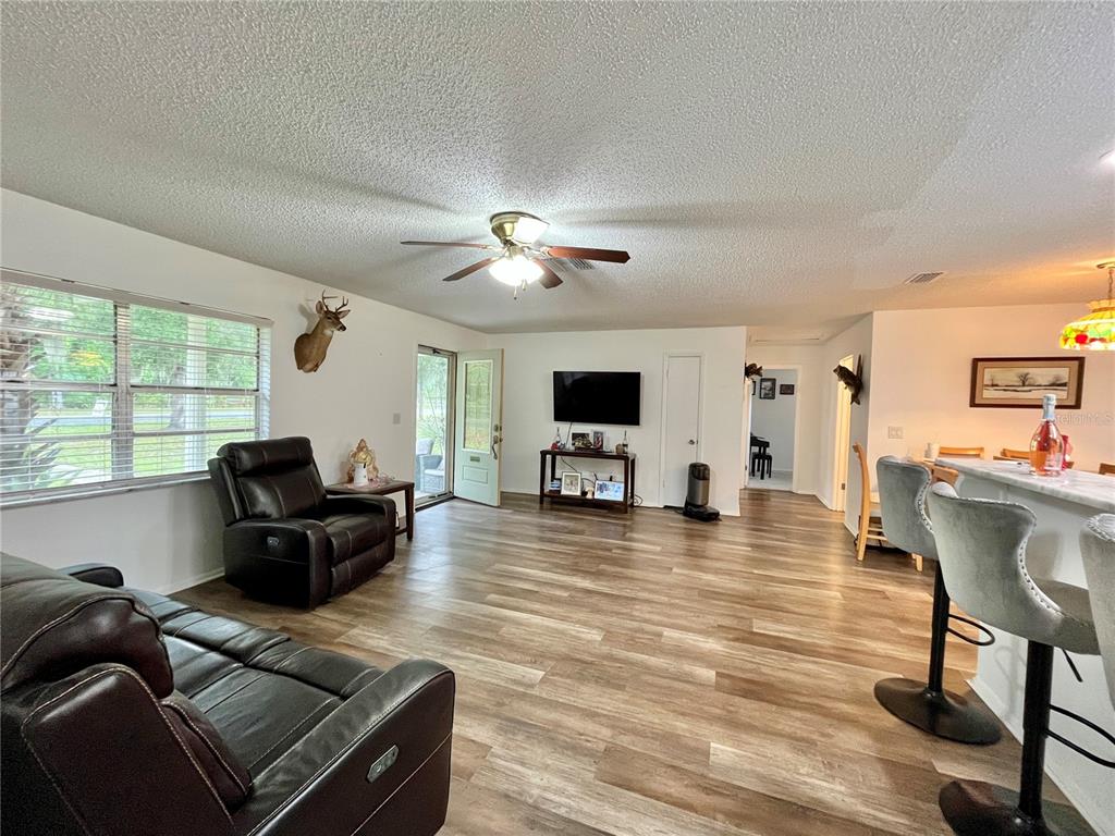 A living room features wood-look flooring, a ceiling fan, a television, and a kitchen bar — 407 POINSETTIA AVENUE, FRUITLAND PARK, FL