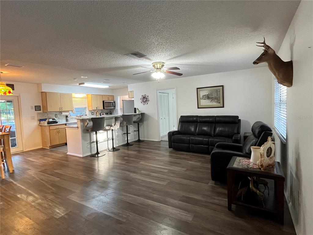 A living room with wood-look flooring, a black leather sofa, and an open kitchen area — 407 POINSETTIA AVENUE, FRUITLAND PARK, FL