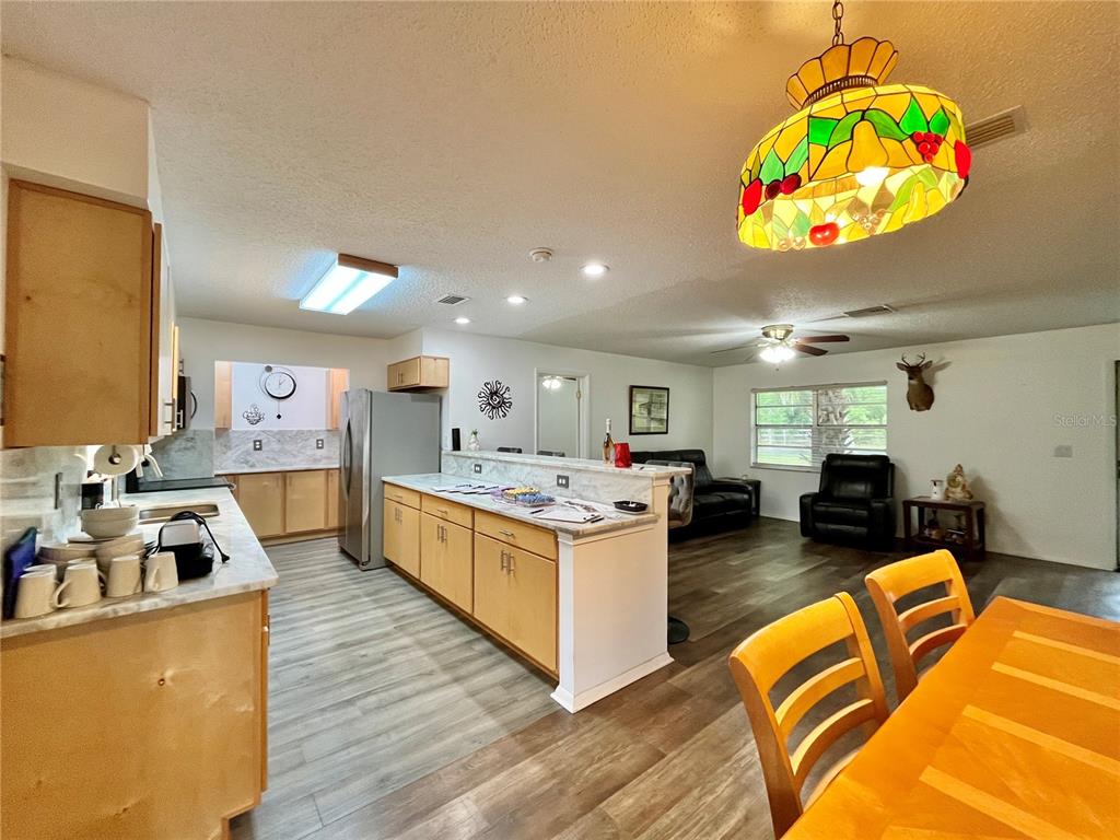 An open-concept kitchen and living area features light wood cabinets, marble-look countertops, and wood flooring — 407 POINSETTIA AVENUE, FRUITLAND PARK, FL