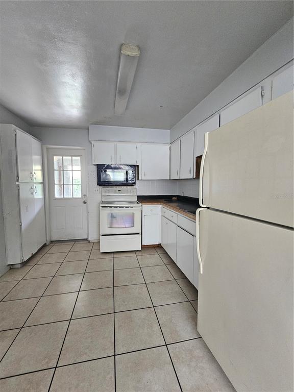 A kitchen features white cabinetry, white appliances, tiled flooring, and a door leading outside — 1212 W MARJORIE STREET, LAKELAND, FL
