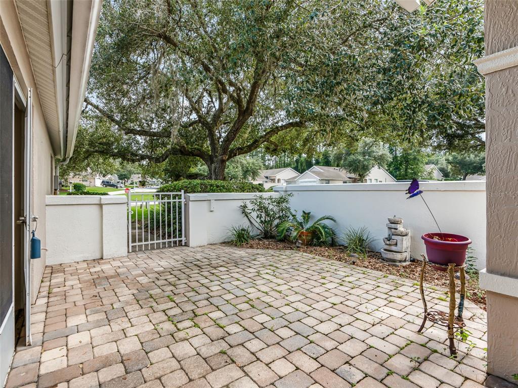 A paved patio features a white wall, a metal gate, and a large shade tree — 7867 SW 115TH LOOP, OCALA, FL