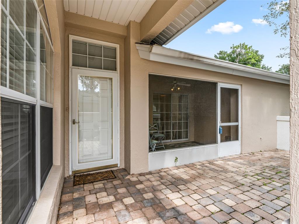 A paved patio area features a white door and a screened-in porch with sliding glass doors — 7867 SW 115TH LOOP, OCALA, FL