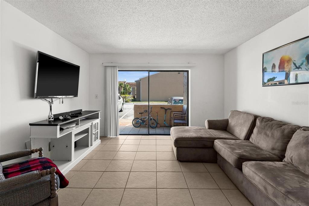 A living room with tile flooring, a sectional sofa, a television, and a sliding glass door — 5201 VINELAND ROAD UNIT 112, ORLANDO, FL