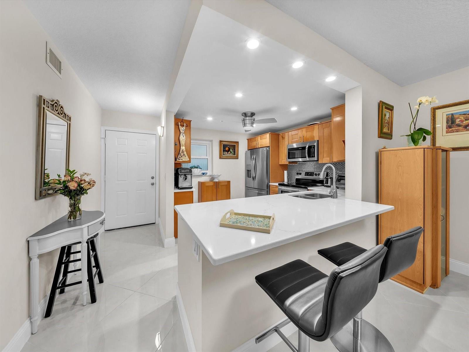 A kitchen features light wood cabinets, a white quartz breakfast bar, and tile flooring — 2515 NE 1st Court # 314, Boynton Beach FL 33435, BOYNTON BEACH, FL